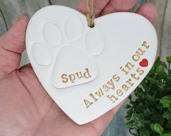 May include: White ceramic heart-shaped ornament with a paw print and the name "Spud" inscribed in gold lettering. The ornament also has the text "Always in our hearts" inscribed in gold lettering with a small red heart.
