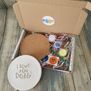 Puede incluir: Un kit de manualidades para hacer un posavasos personalizado. El kit incluye un posavasos de cer&aacute;mica blanca con las palabras "i love you Daddy" en relieve, un posavasos de corcho, pintura, pinceles y pegatinas.
