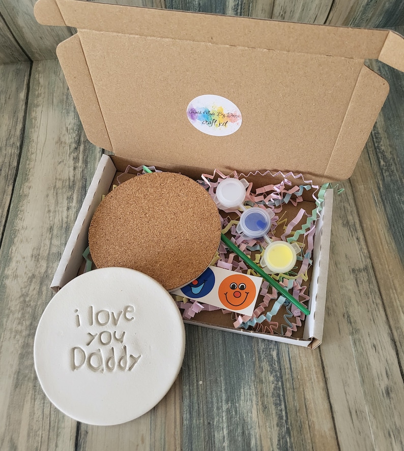 Puede incluir: Un kit de manualidades para hacer un posavasos personalizado. El kit incluye un posavasos de cer&aacute;mica blanca con las palabras "i love you Daddy" en relieve, un posavasos de corcho, pintura, pinceles y pegatinas.