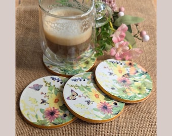 May include: A clear glass mug filled with coffee sits on a floral coaster. Three additional coasters with a similar design are visible. The coasters feature a watercolor design of yellow sunflowers, purple flowers, green leaves, and butterflies, with a gold edge.