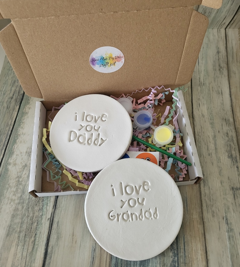 Puede incluir: Un kit de manualidades con dos posavasos de cer&aacute;mica blanca, uno con el texto "Te quiero pap&aacute;" y el otro con el texto "Te quiero abuelo". El kit incluye pintura, un pincel y una pegatina.