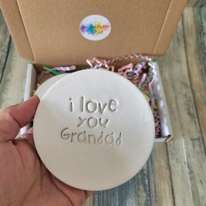 Puede incluir: Posavasos de cer&aacute;mica blanca con el texto "i love you Granddad" en relieve en la superficie.
