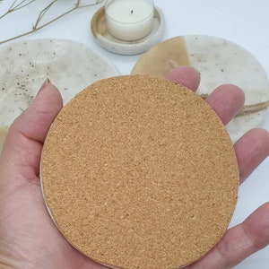 May include: A round cork coaster with a light brown color. The coaster is made of natural cork and has a slightly rough texture.