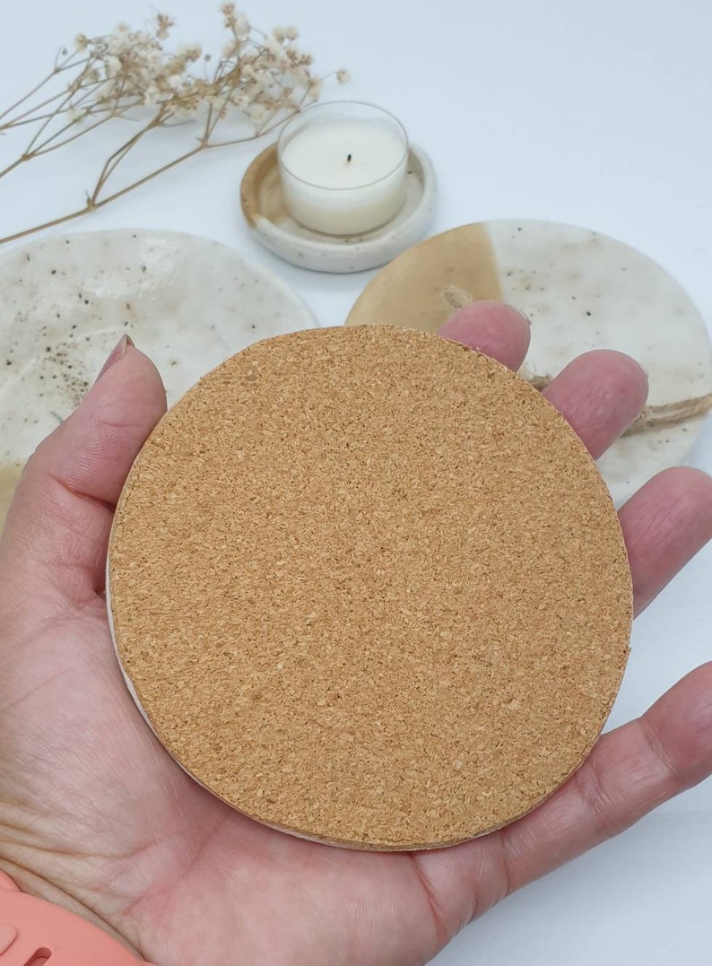 May include: A round cork coaster with a light brown color. The coaster is made of natural cork and has a slightly rough texture.