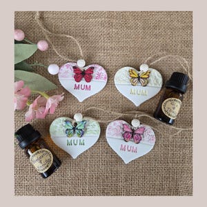 May include: Four white ceramic heart-shaped ornaments with butterfly designs and the word "MUM" on each. Two bottles of essential oil are also pictured.