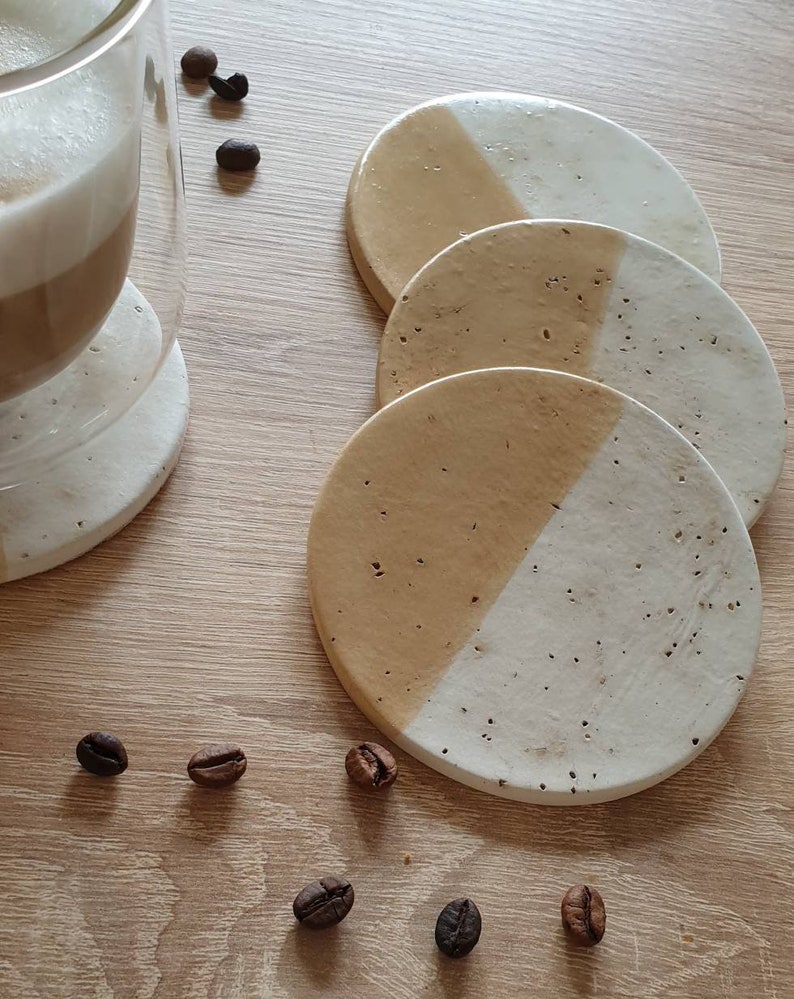 May include: Set of four round coasters with a beige and white speckled design. Each coaster is divided in half, with one half beige and the other half white.