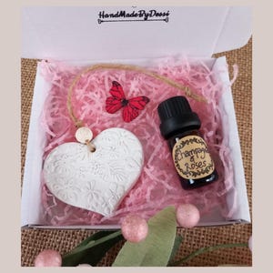 May include: A white ceramic heart-shaped diffuser with a floral design, a small bottle of essential oil labelled "Champagne & Roses", and a red butterfly charm in a pink and white gift box.