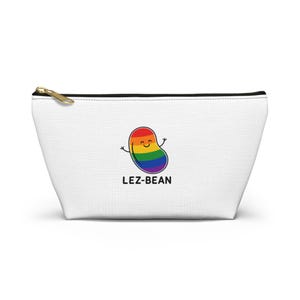 May include: White canvas pouch with a gold zipper. The pouch features a cartoon bean in rainbow colors with a smiling face and the text "LEZ-BEAN" in black. The pouch is a fun and colorful accessory.