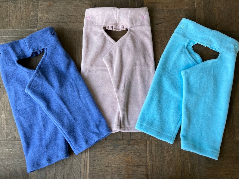 May include: Three fleece fabric neck gaiters in different colors: blue, pink, and light blue. Each gaiter has a heart-shaped opening in the front.