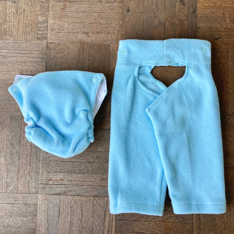 May include: Two light blue fleece baby items. One is a diaper cover with a white trim and the other is a pair of pants with a cutout in the back.