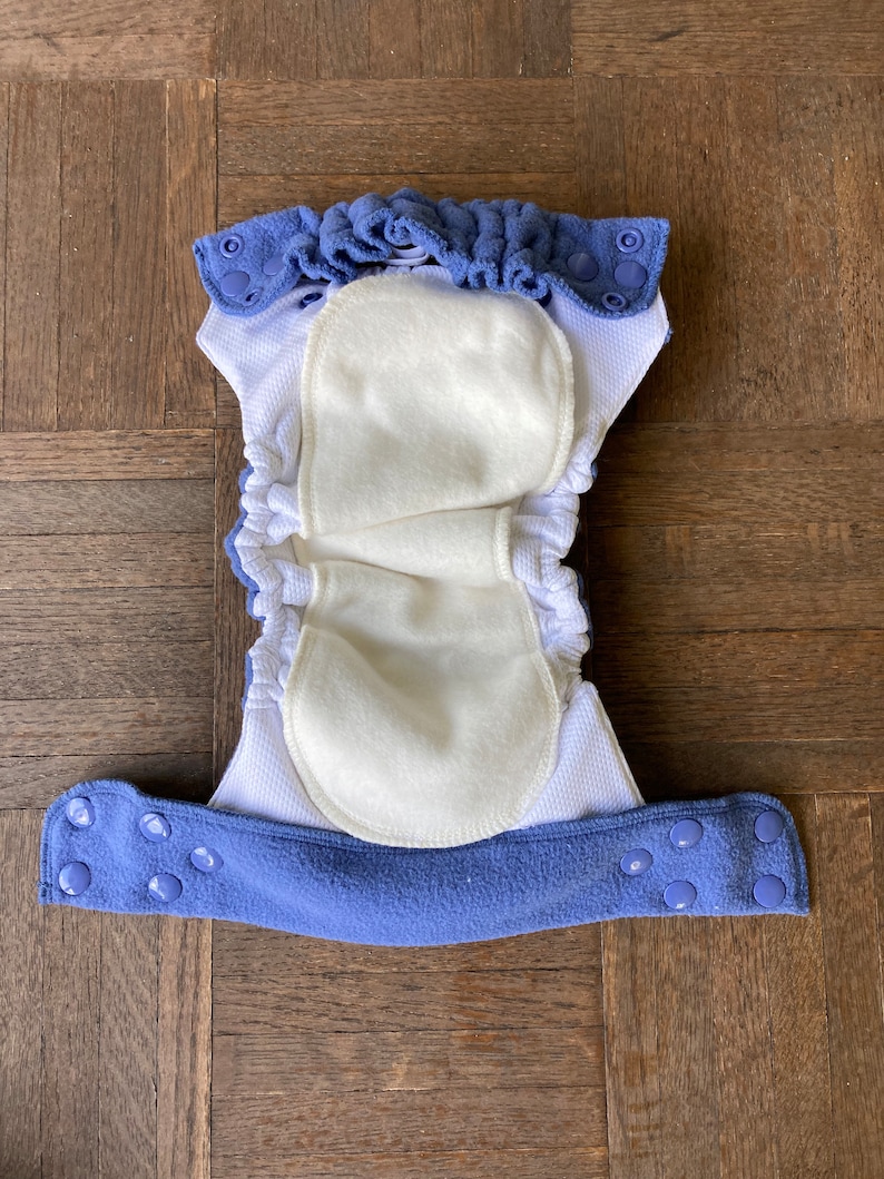 May include: A blue and white reusable cloth diaper with a white fleece lining and snap closures.