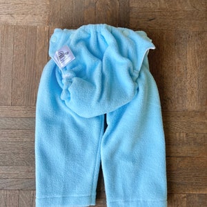 May include: A light blue fleece baby pants with a white label that says "BabyLegs, Inc."