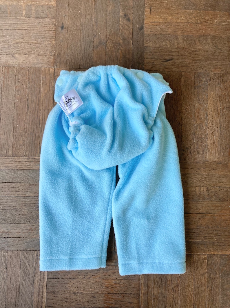 May include: A light blue fleece baby pants with a white label that says "BabyLegs, Inc."