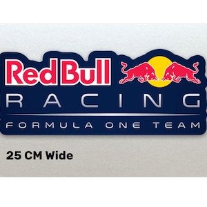May include: A rectangular sticker with the Red Bull Racing Formula One Team logo. The design features the words "Red Bull Racing" in red and white, and two red bulls. The sticker is 25 cm wide.