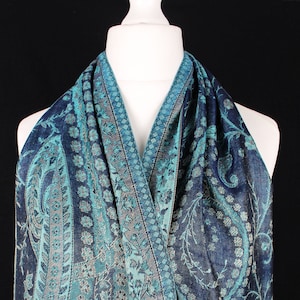 May include: A teal and navy blue paisley patterned scarf with a silver metallic thread woven into the design. The scarf is draped over a white mannequin.
