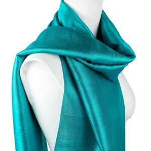 May include: A teal blue silk scarf draped over a white mannequin. The scarf is soft and flowing, with a subtle sheen.