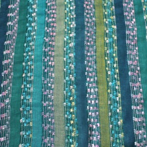 May include: A fabric featuring vertical stripes in shades of dark green, teal, and olive. The pattern includes alternating bands of solid color and textured, semi-sheer sections woven with small, colorful flecks of pink, yellow, and light blue thread.