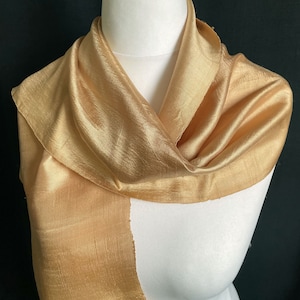 May include: A gold silk scarf with a smooth, shiny texture. The scarf is draped over a white mannequin.