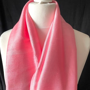 May include: A soft pink silk scarf draped over a white mannequin. The scarf is made of a smooth, luxurious fabric and has a subtle sheen.