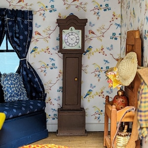 Può includere: Un orologio a pendolo marrone con un quadrante bianco e numeri romani neri. L'orologio si trova in un ambiente di casa delle bambole con un divano blu e una carta da parati floreale.