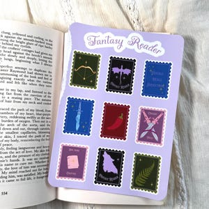 Op de afbeelding: Een stickervel met een lichtpaarse achtergrond en de tekst Fantasy Reader bovenaan. Het bevat negen rechthoekige stickers in postzegelstijl met illustraties van een boog, draak, dolk, chilipeper, zwaarden, boek, wolf en een varenblad.