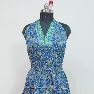 Könnte beinhalten: Blaues Neckholder-Kleid mit Paisley-Muster und grünen Verzierungen. Das Kleid wird auf einer Schaufensterpuppe präsentiert. Das Kleid hat ein figurbetontes Oberteil und einen Stufenrock. Das Kleid ist ca. 140 cm lang.