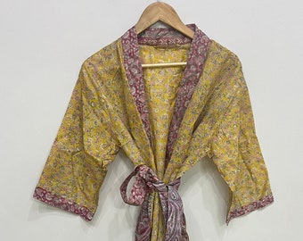 May include: A yellow floral print robe with a contrasting paisley print trim and belt. The robe is hanging on a wooden hanger against a white background. The robe's design features a yellow base with a delicate floral pattern, complemented by a deep burgundy paisley trim.