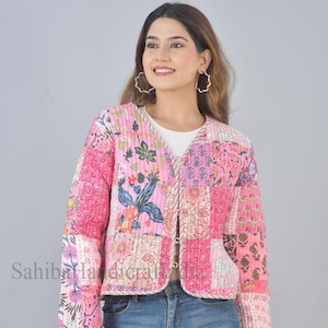 May include: A pink quilted jacket with a floral patchwork design. The jacket has a V-neck and long sleeves. It is cropped and has a button closure.