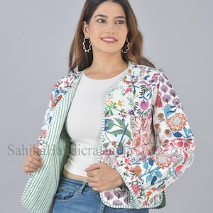 Może przedstawiać: Biała pikowana kurtka z kwiatowym nadrukiem i zielonym wykończeniem. Kurtka ma kołnierz typu „mandarynka” i długie rękawy. Modelka ma na sobie biały t-shirt i niebieskie dżinsy.