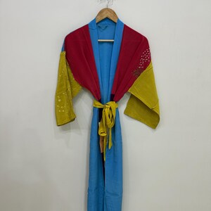 Puede incluir: Una bata de manga larga con un diseño de bloques de color en azul brillante, rojo intenso y amarillo mostaza. La prenda incluye un cinturón a juego en amarillo mostaza en la cintura y muestra sutiles patrones de puntos blancos en las secciones.