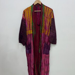May include: A long-sleeved kimono robe featuring a vibrant tie-dye pattern in shades of magenta, mustard yellow, deep purple, and green. The garment has an open front design, a shawl collar, and two patch pockets on the lower front section.