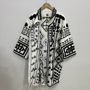 May include: A white kimono with black embroidered geometric patterns. The kimono has a collar and short sleeves.