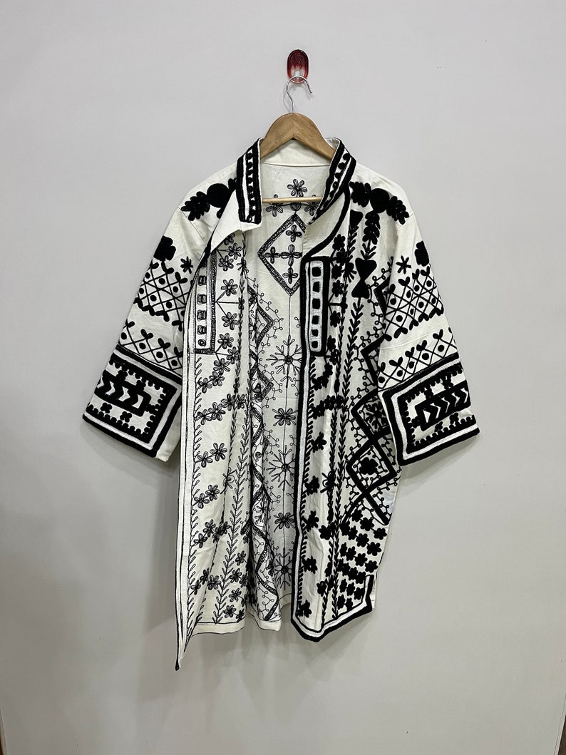 May include: A white kimono with black embroidered geometric patterns. The kimono has a collar and short sleeves.