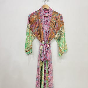 May include: A long-sleeved robe featuring a vibrant, multi-colored paisley pattern in shades of pink, green, orange, and purple. The garment includes a matching fabric tie belt at the waist, an open front design, and wide sleeves, all hanging on a wooden hanger.