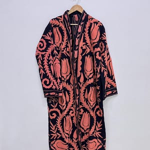 Op de afbeelding: Een lange zwarte robe met een roze bloemenborduursel. De robe heeft lange mouwen en een shawlkraag.