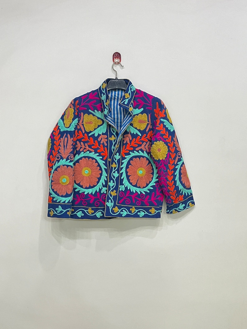 May include: A blue embroidered jacket with floral patterns in shades of pink, orange, yellow, and green. The jacket has a button closure and long sleeves.