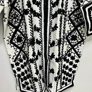 May include: A white cotton tunic with black embroidery featuring a geometric pattern and floral designs.