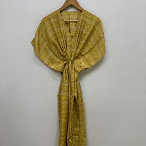 May include: A mustard yellow kaftan featuring a V-neckline and short, wide sleeves. The garment is decorated with a repeating pattern of horizontal stripes and geometric motifs, and includes a drawstring waist tie for a cinched silhouette.
