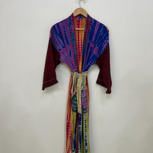 May include: A colorful tie-dye robe with long sleeves, hanging on a wooden hanger. The robe features a vibrant mix of blue, purple, pink, yellow, and green hues. The sleeves are a deep burgundy color, and a matching tie belt is included.