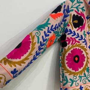 May include: A pink embroidered jacket with colorful floral patterns. The jacket has long sleeves and a button-up front.