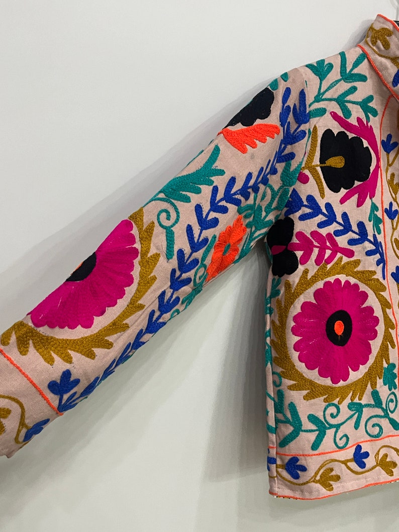 May include: A pink embroidered jacket with colorful floral patterns. The jacket has long sleeves and a button-up front.