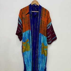 May include: A long-sleeved kimono robe featuring a vibrant tie-dye pattern in shades of orange, bright blue, deep purple, and mustard yellow. The garment includes two front patch pockets, a solid blue trim along the opening, and side slits.