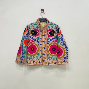 May include: A beige embroidered jacket with a floral pattern in shades of pink, blue, green, orange, and black. The jacket has a mandarin collar and a button closure.