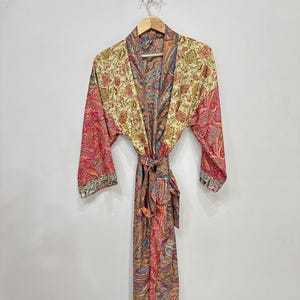 Könnte beinhalten: Ein langärmeliger Morgenmantel mit einem lebendigen Paisley-Muster in Rot-, Gelb-, Grün- und Blautönen. Das Kleidungsstück verfügt über einen passenden Bindegürtel in der Taille, einen Schalkragen und ein buntes Blumen- und Paisley-Design.