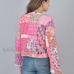 Op de afbeelding: Een roze gewatteerd jack met een bloemig patchwork-ontwerp. Het jack heeft een ronde hals en lange mouwen.