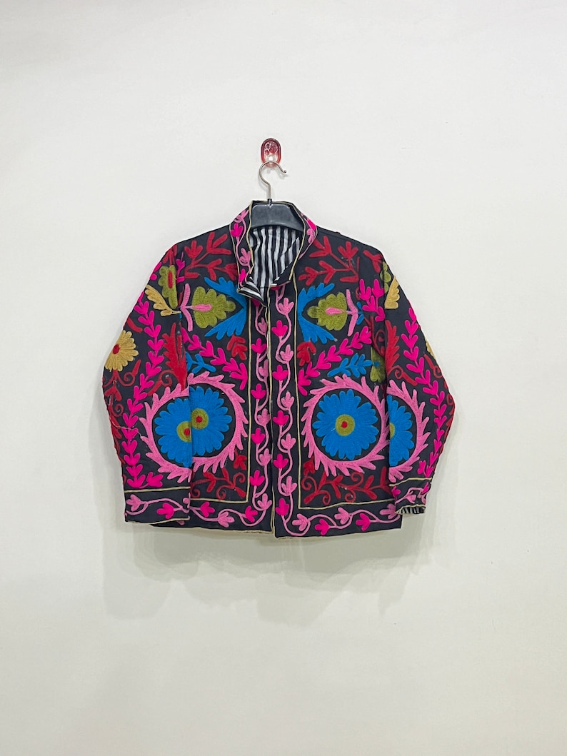 May include: A black embroidered jacket with pink, blue, green, and yellow floral patterns. The jacket has a striped lining and a button closure.