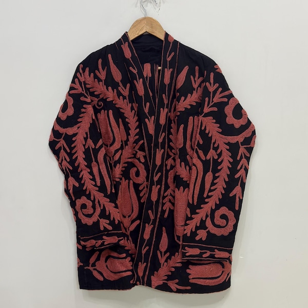 May include: Black jacket with a red floral pattern. The jacket is hanging on a wooden hanger. The floral design covers the entire jacket, including the sleeves and front panels. The jacket is made of a soft material.