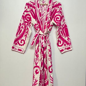 Puede incluir: Una bata blanca con un estampado floral rosa. La bata tiene mangas largas y un cintur&oacute;n de atar.