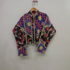 Könnte beinhalten: Eine kurz geschnittene Jacke mit Patchwork-Design, bestehend aus verschiedenen Blumen- und geometrischen Mustern in den Farben Violett, Blau, Rot, Gelb und Schwarz. Das Kleidungsstück hat lange Ärmel, einen Stehkragen und weiße Steppnähte.