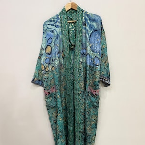 May include: A long-sleeved kimono robe featuring a vibrant teal and blue color palette with a complex pattern of floral motifs and abstract shapes. The garment includes a matching tie belt, two front pockets, and a shawl collar design.